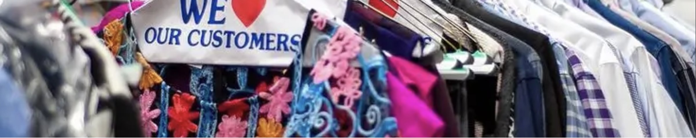 Freshly cleaned garments on the rack at a Blue Sky shop, under a We Love Our Customers sign